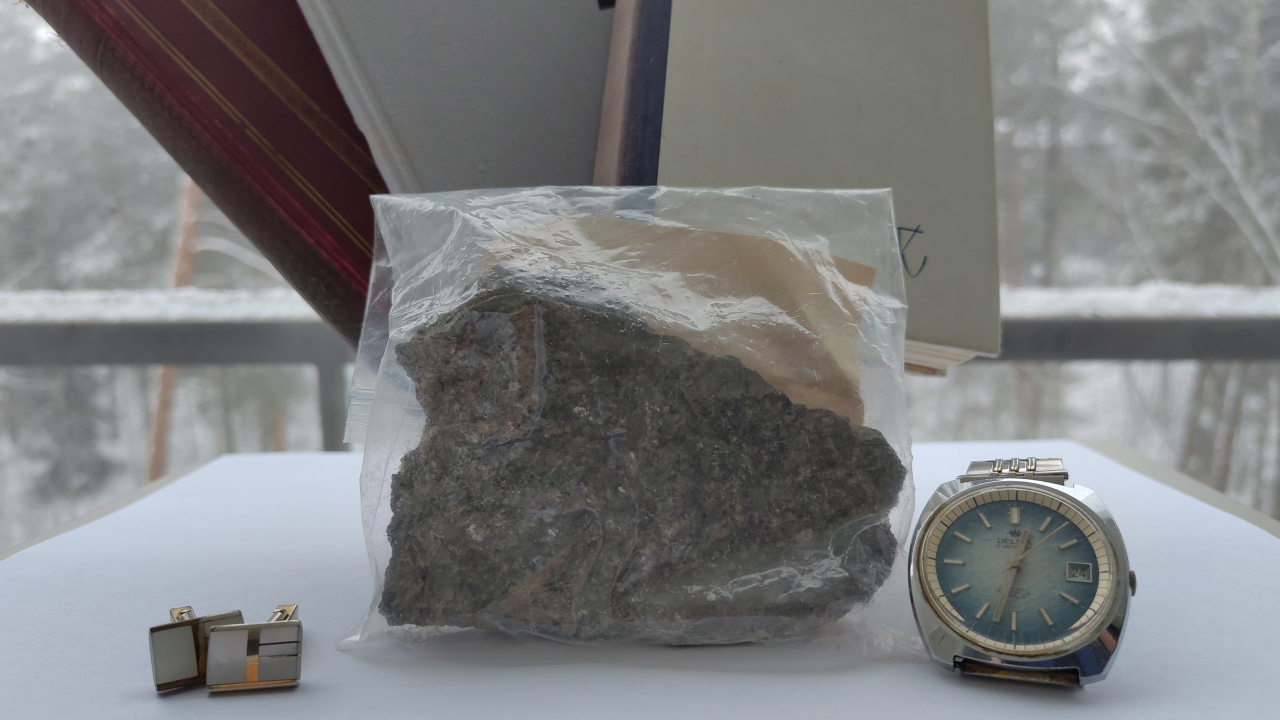 Some items I mention in the post. The cufflinks, a stone and the watch. Behind them there are three books: one dark red and two grey ones. In the background you can see the snowy forest through the balcony.